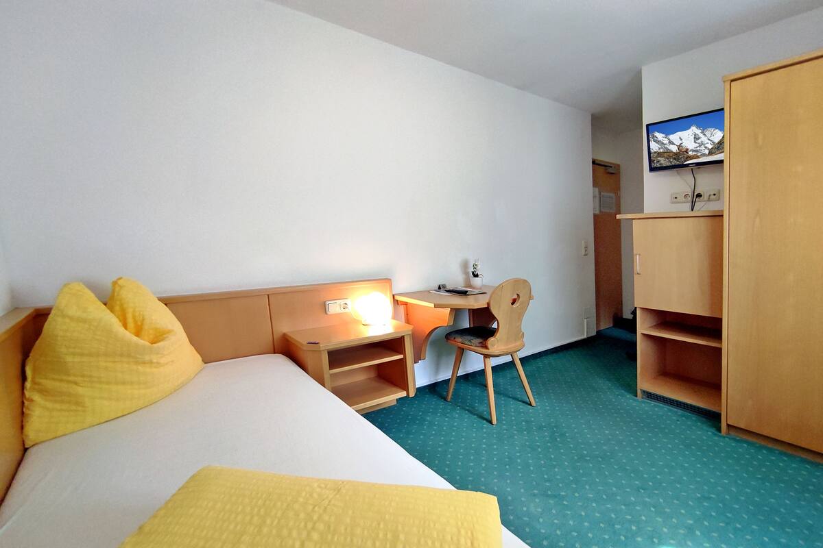 A hotel room with a bed, a desk, a chair, and a wardrobe.