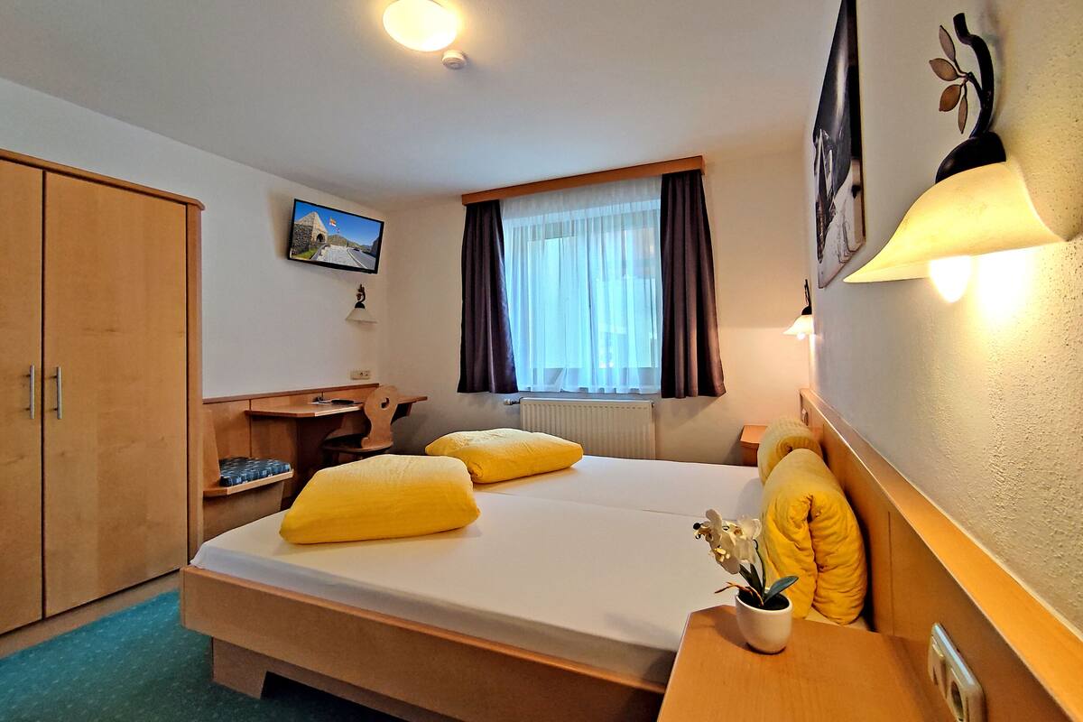 A hotel room with a bed, a desk, a wardrobe, a television, and a window with curtains.