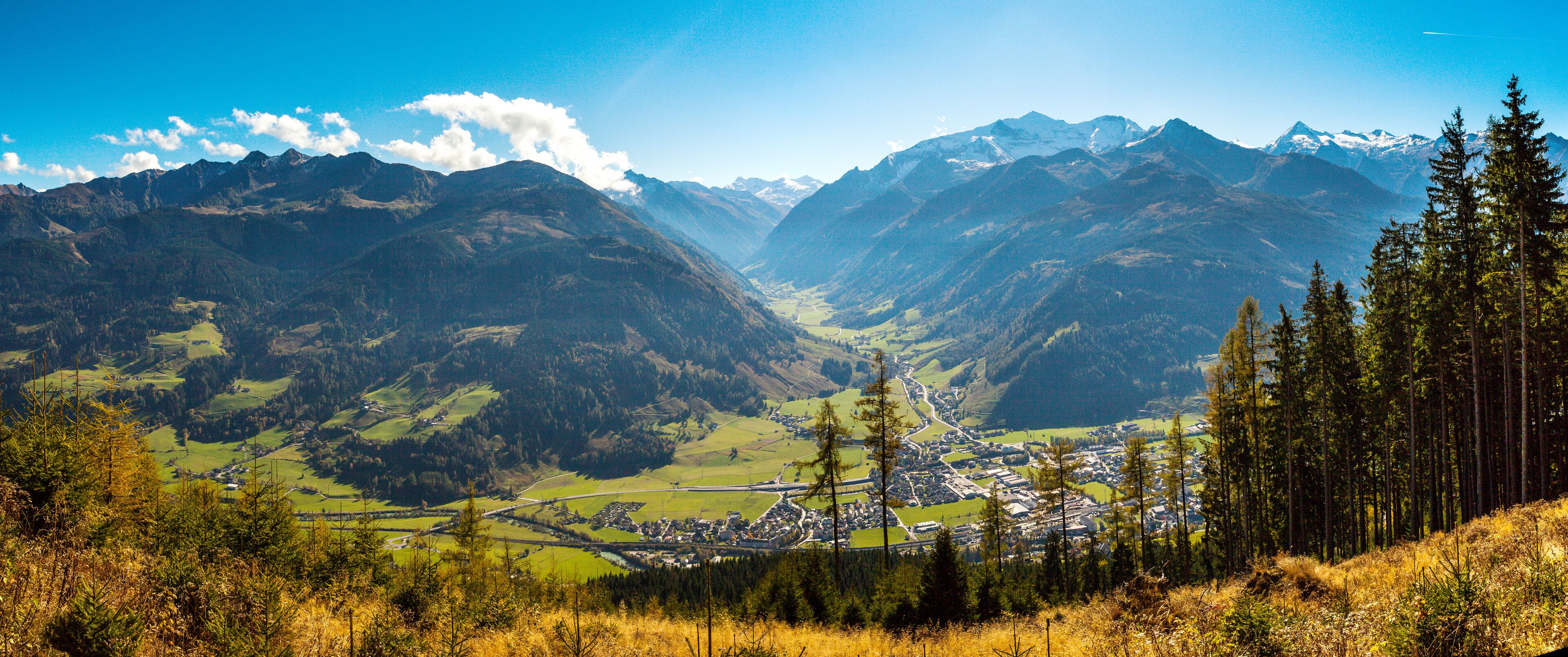 Ein Tal mit Bergen im Hintergrund und einer Stadt in der Mitte, vor der ein bewaldetes Gebiet liegt.