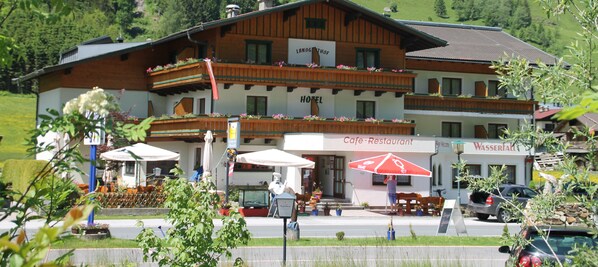 A hotel with a wooden facade, balconies, and outdoor seating. - Hotel Wasserfall (Fusch an der Grossglocknerstrasse)