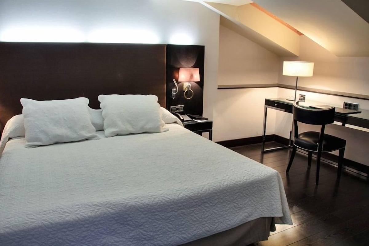 Una habitación de hotel con una cama grande, un escritorio con silla y una lámpara.