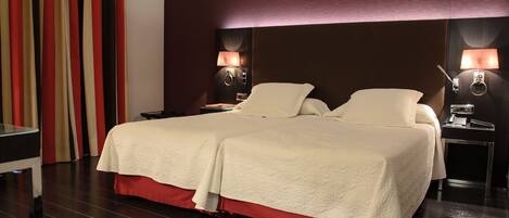 A double bed with a red skirt, two bedside tables, and two wall-mounted lamps.