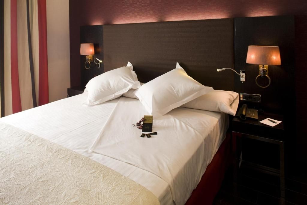A hotel room with a large bed, two bedside lamps, a nightstand with a phone, and a decorative item on the bed.