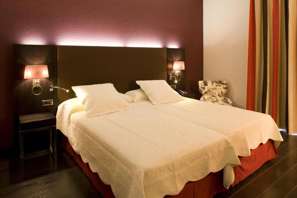 A hotel room with a large bed, two bedside lamps, a nightstand, and a chair.