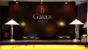 Un comptoir d’accueil à l’hôtel II Garesus, avec un panneau mural en bois foncé, deux lampes et un bureau d’accueil.