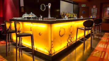 Una zona de bar con mostrador de mármol, taburetes y barra bien iluminada.