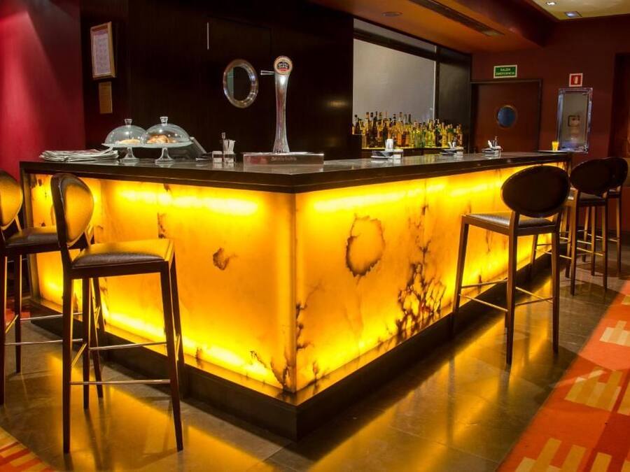 Una zona de bar con mostrador de mármol, taburetes y barra bien iluminada.