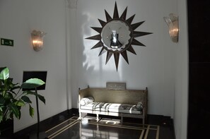 A lobby with a sunburst mirror, a bench, a potted plant, and a wall-mounted light fixture. - Hotel Boutique Gareus (Valladolid)