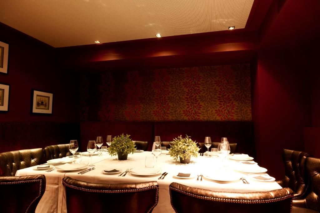 A round dining table with white tablecloth, surrounded by leather chairs, in a dimly lit room with a patterned wall and ceiling.