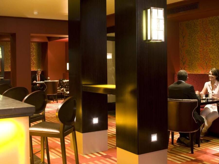Un restaurante con zona de bar, disposición de mesas y pared con diseño.