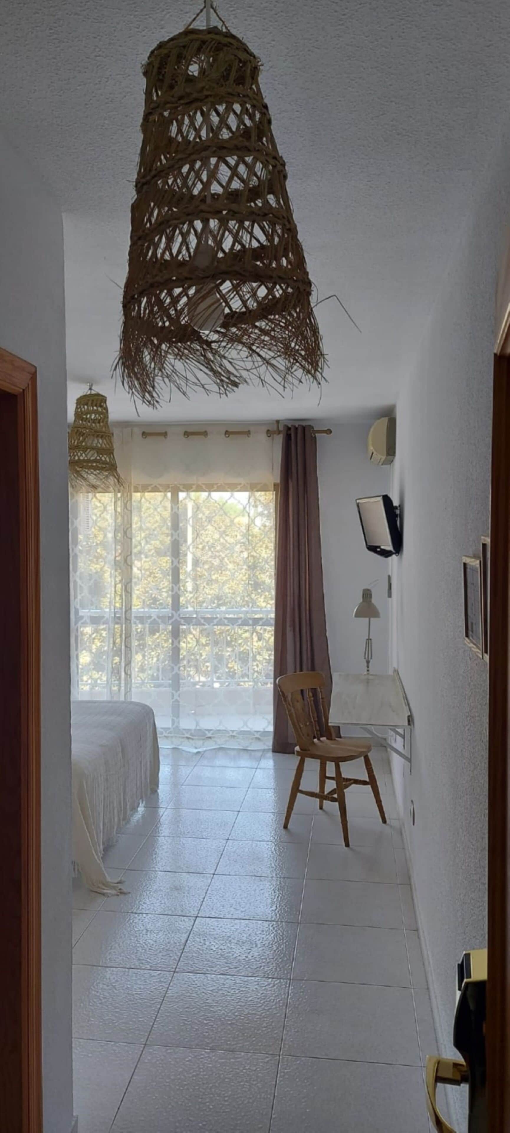 A room with a bed, a chair, a desk, a lamp, and a hanging light fixture.