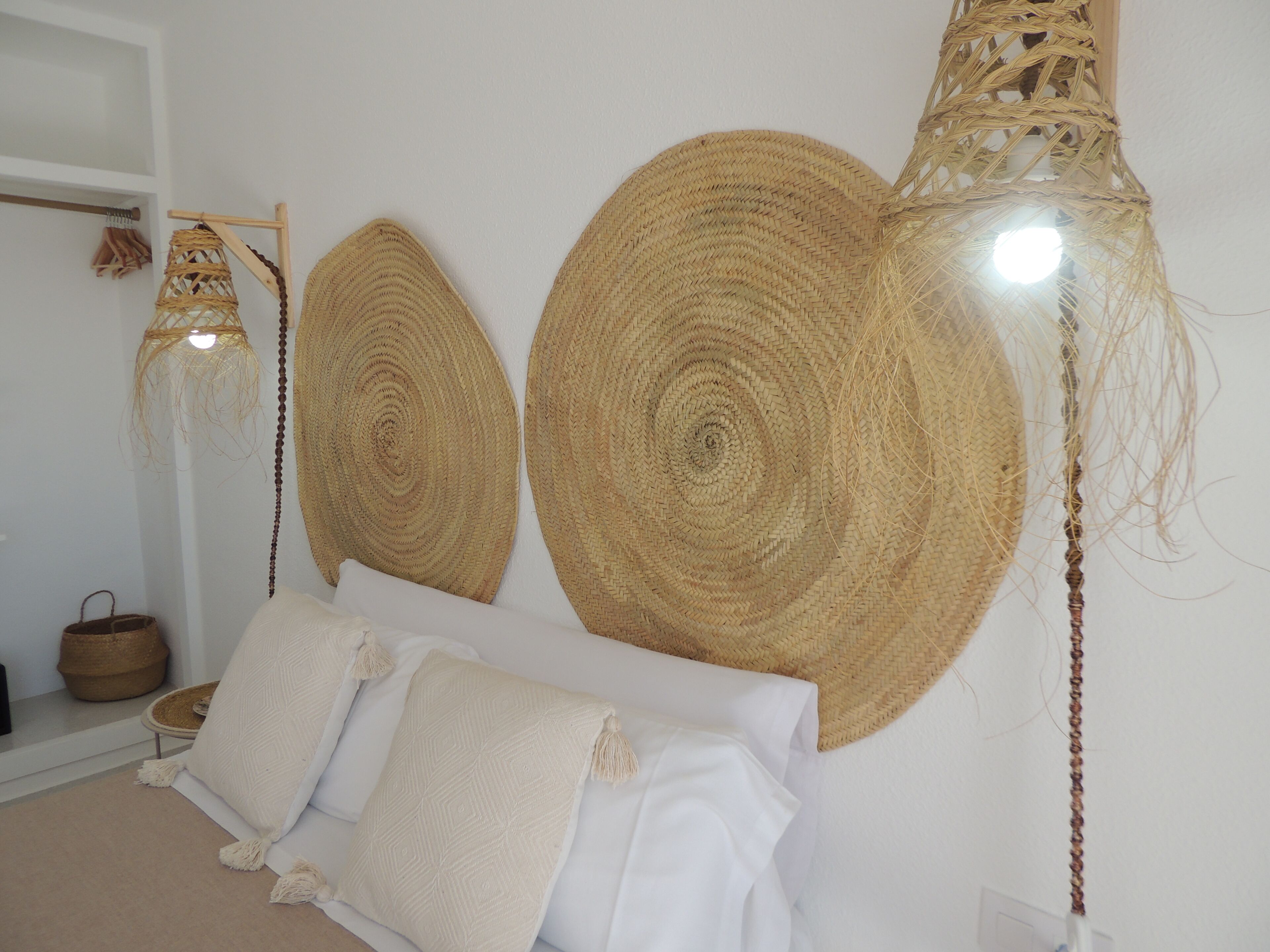 A room with a bed, two large woven wall hangings, a hanging light fixture, and a woven basket on a shelf.