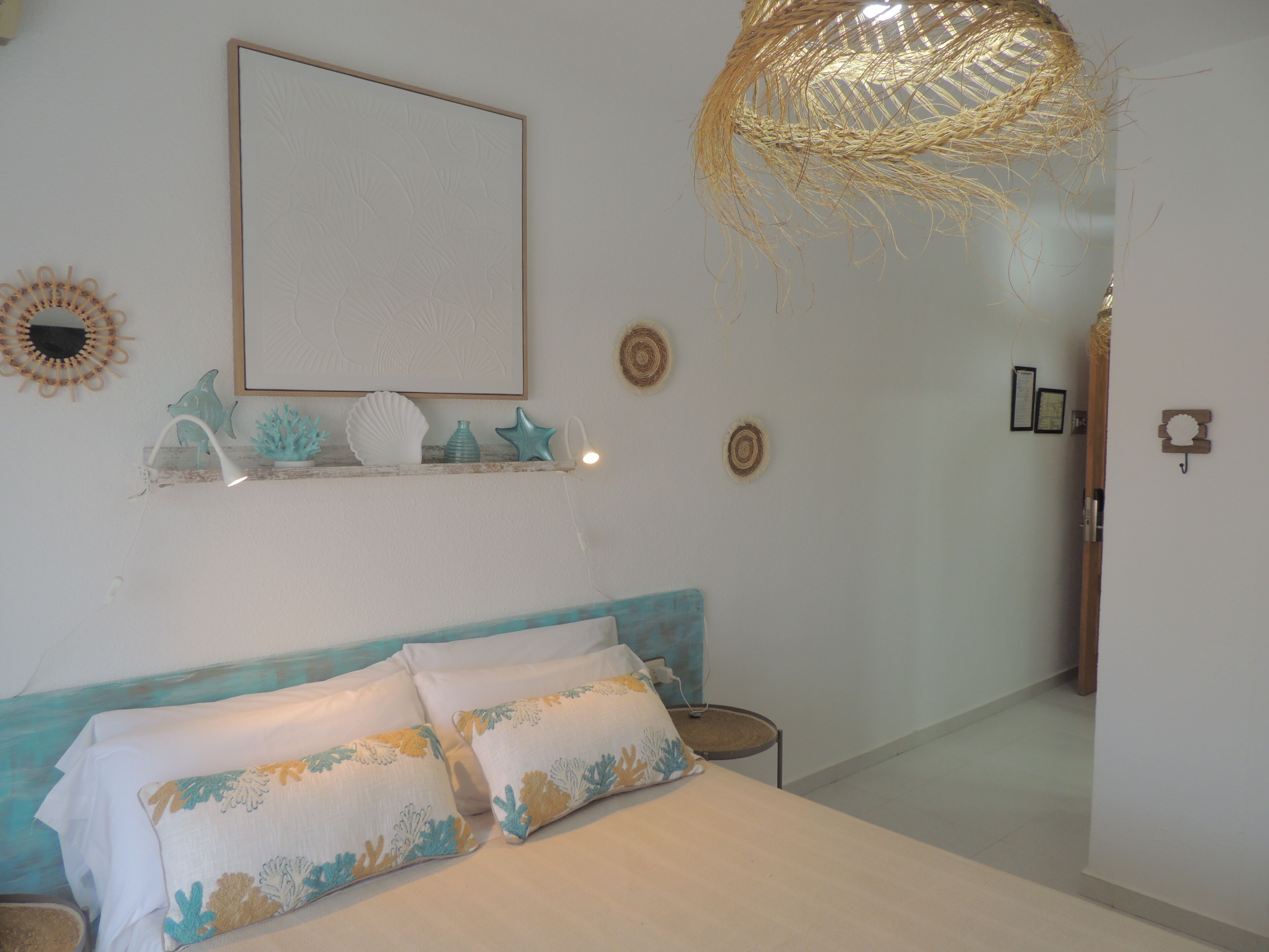Quarto com cama, prateleira com objetos decorativos, quadro na parede e luminária de tecido.