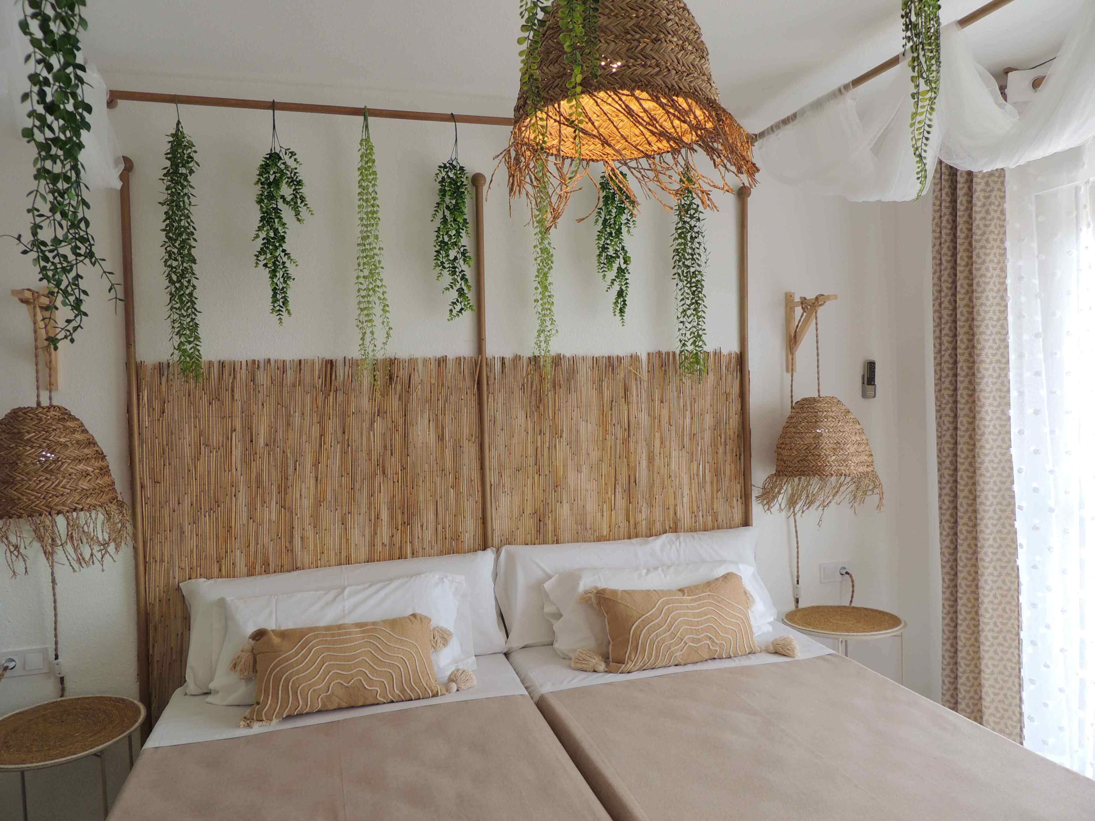 A bedroom with a large bed, two bedside tables, hanging plants, and a woven headboard.