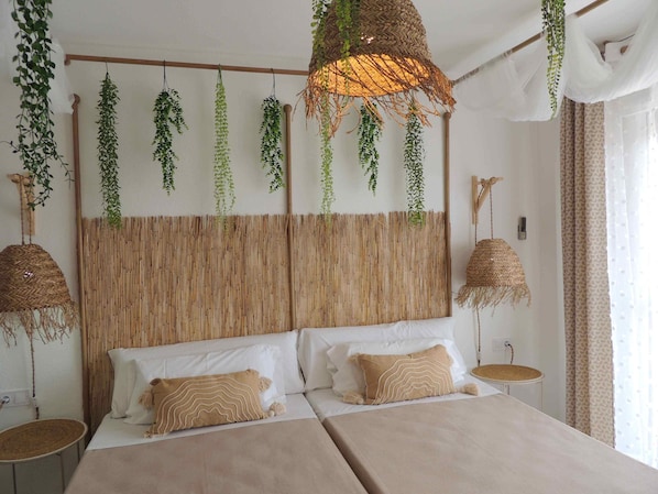 Un dormitorio con una cama grande, dos mesitas de noche, plantas colgantes y un cabecero tejido.