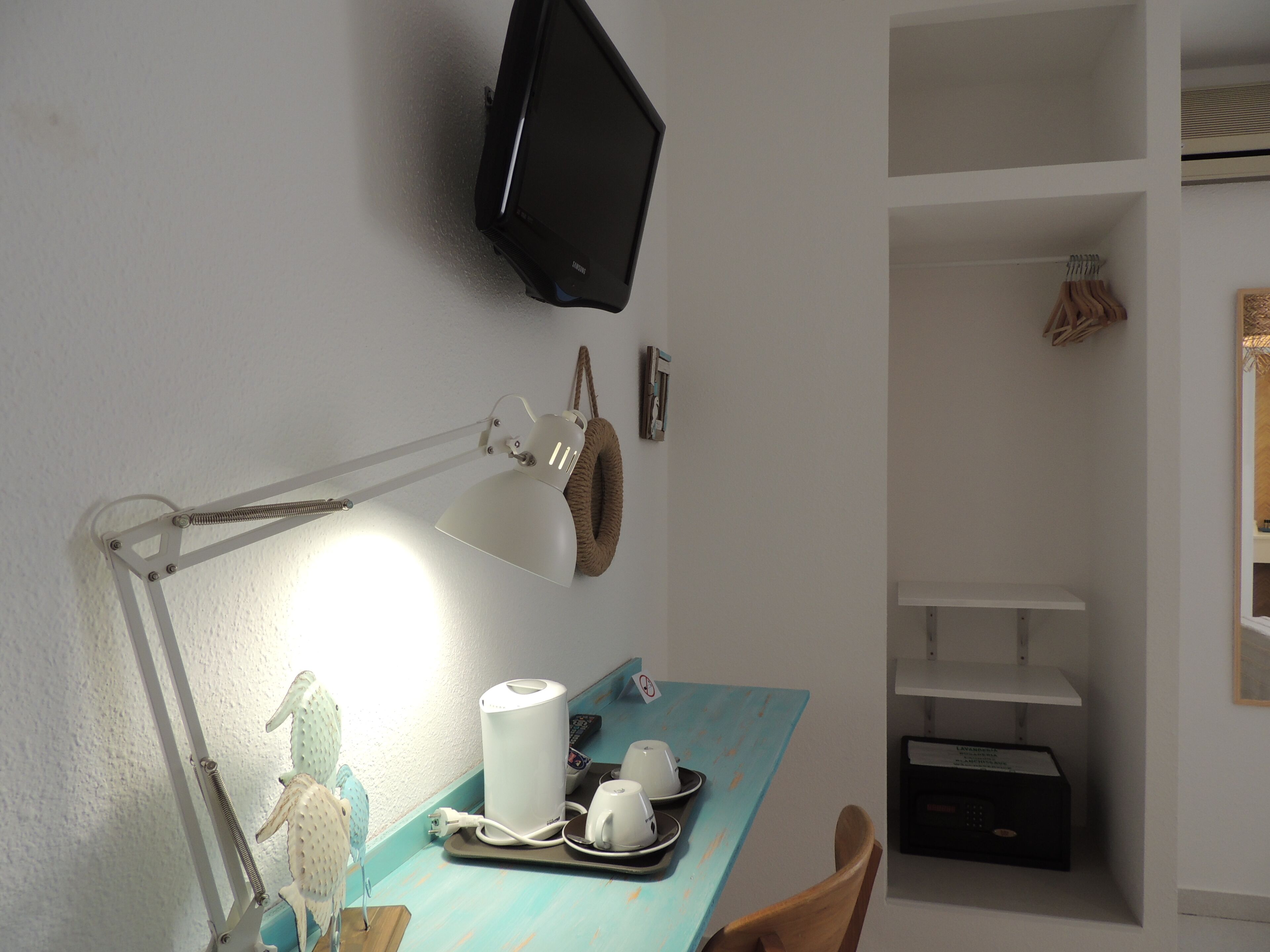 Een werkplek met een bureaulamp, een flatscreen televisie aan de muur en een dienblad met bekers en een afstandsbediening.
