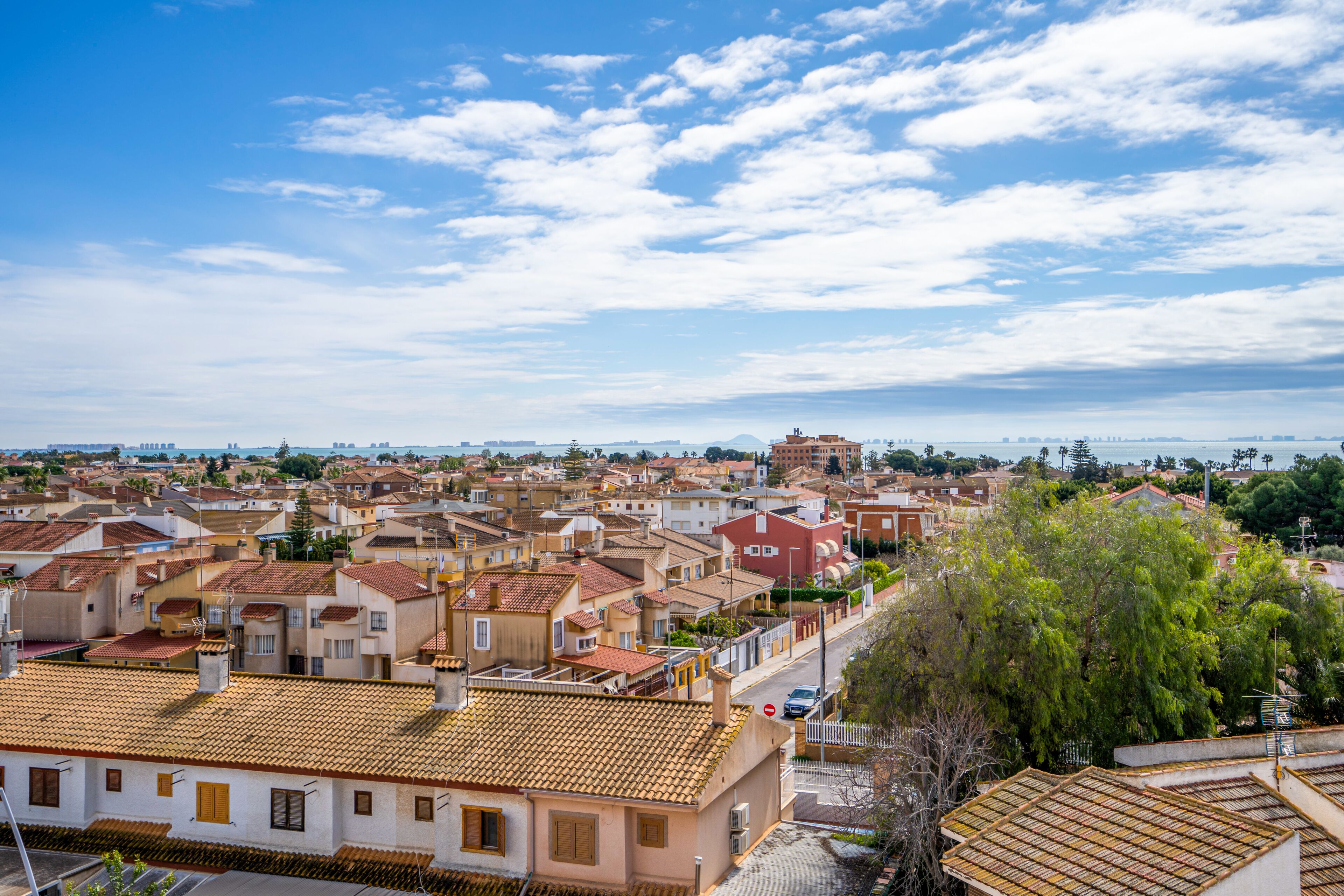A residential area with terracotta-tiled roofs, a mix of building styles, and a clear sky.