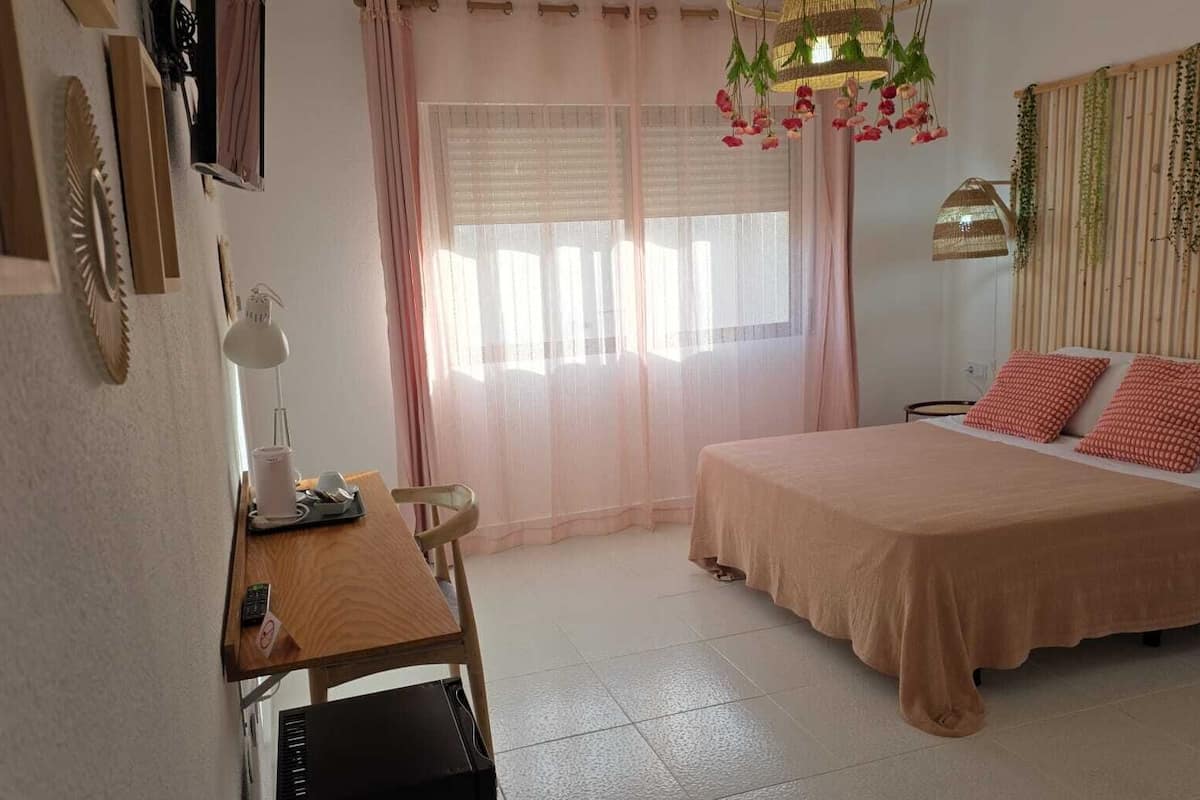 Un dormitorio con cama, escritorio, silla, lámpara y ventana con cortinas.