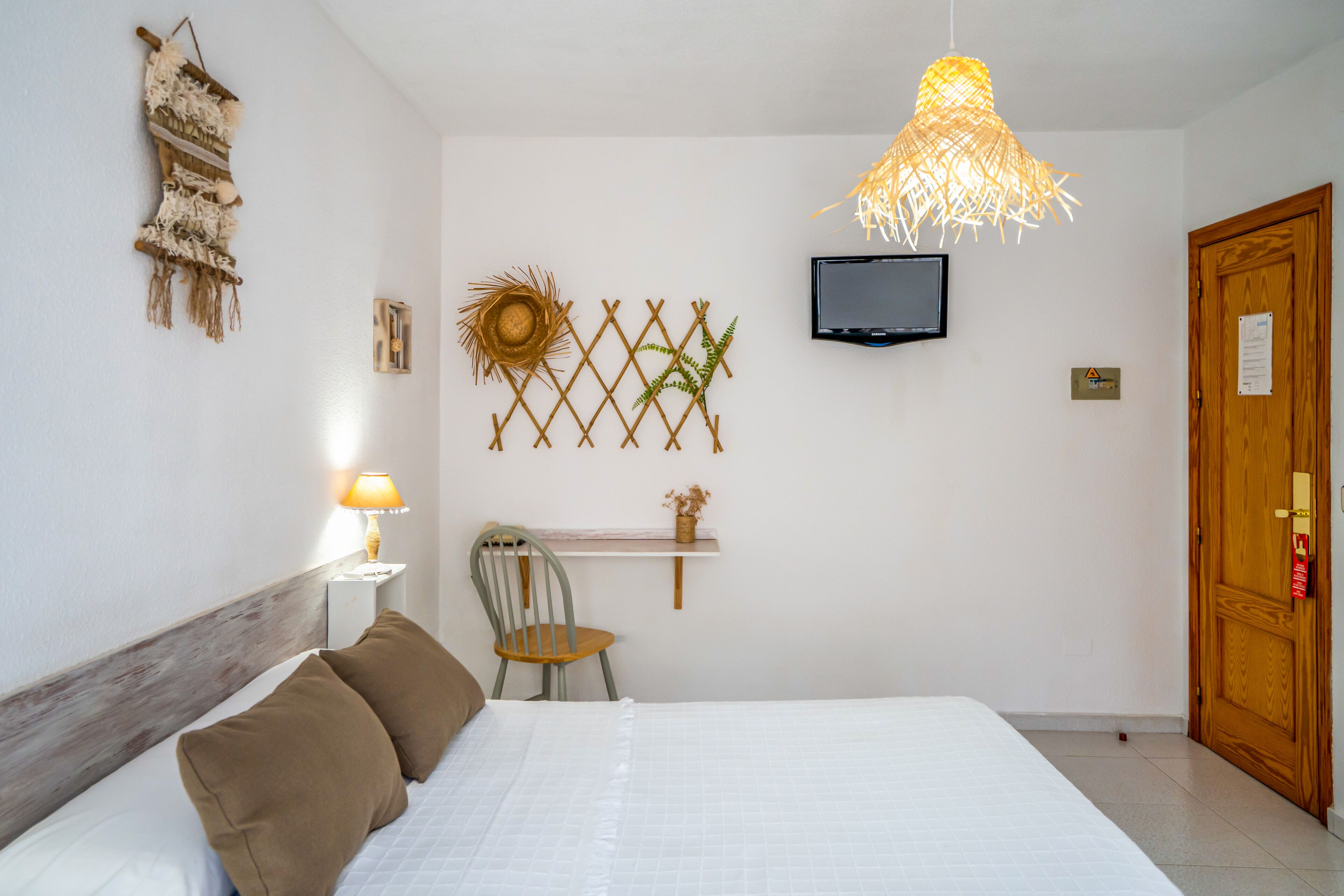 Un dormitorio con cama, una silla, televisor y una puerta.