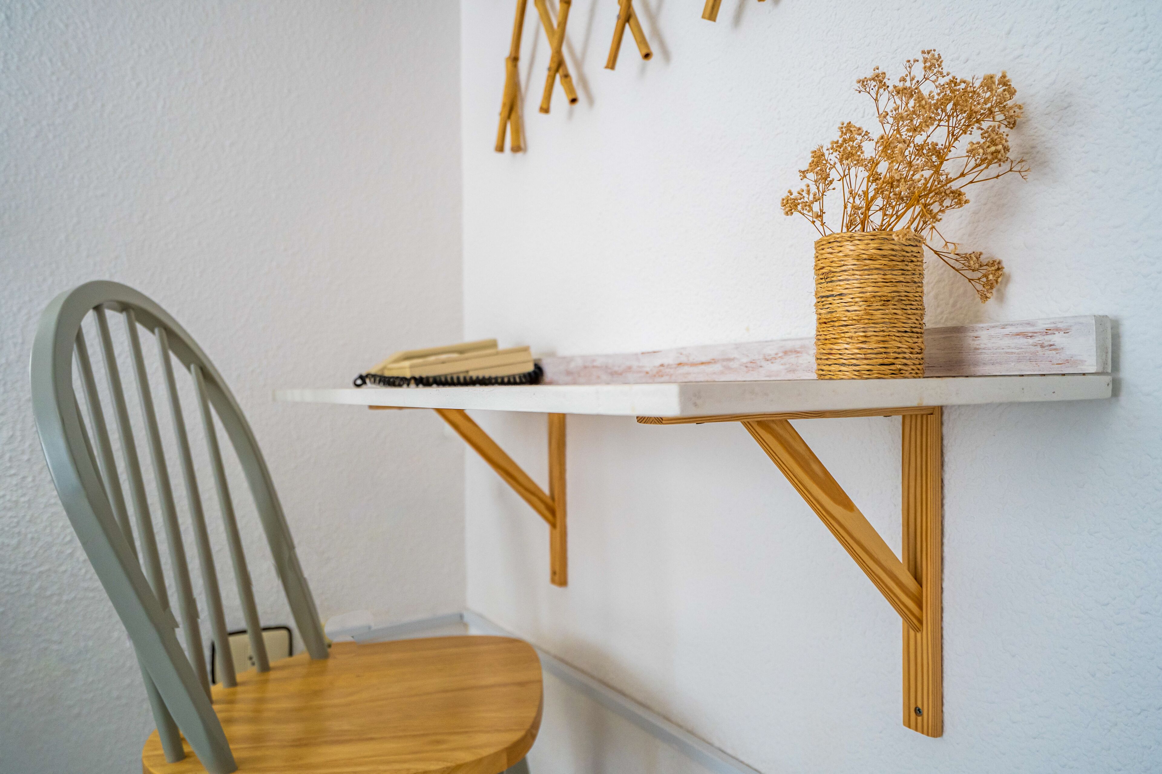 Uma pequena mesa de madeira com uma cesta de palha contendo flores secas, um bloco de notas e uma caneta sobre uma superfície de mármore branco.