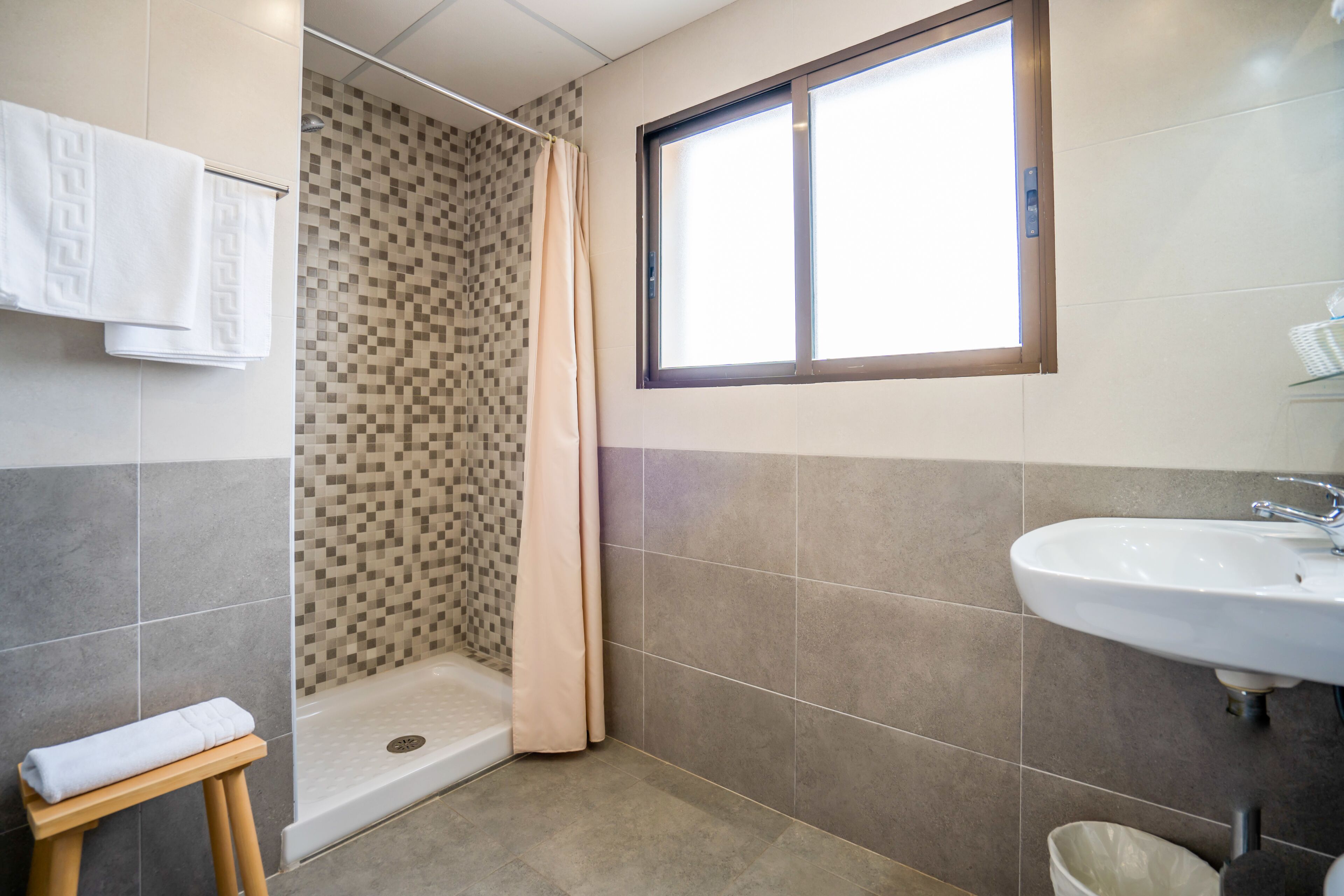A bathroom with a shower, a sink, and a window.