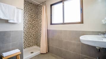 A bathroom with a shower, a sink, and a window.