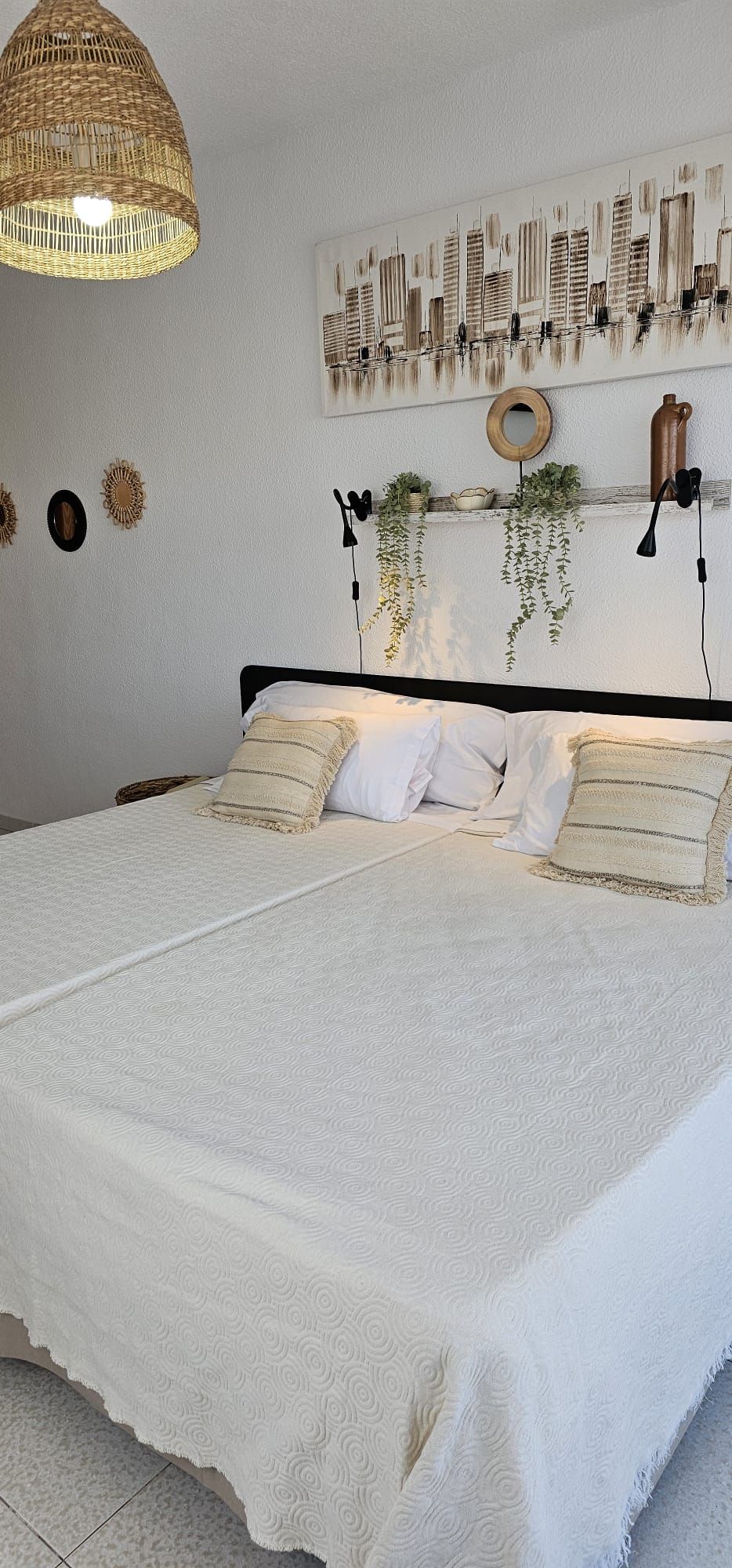 Un dormitorio con una cama grande, una lámpara colgante, un espejo en la pared y una pintura de un paisaje urbano.