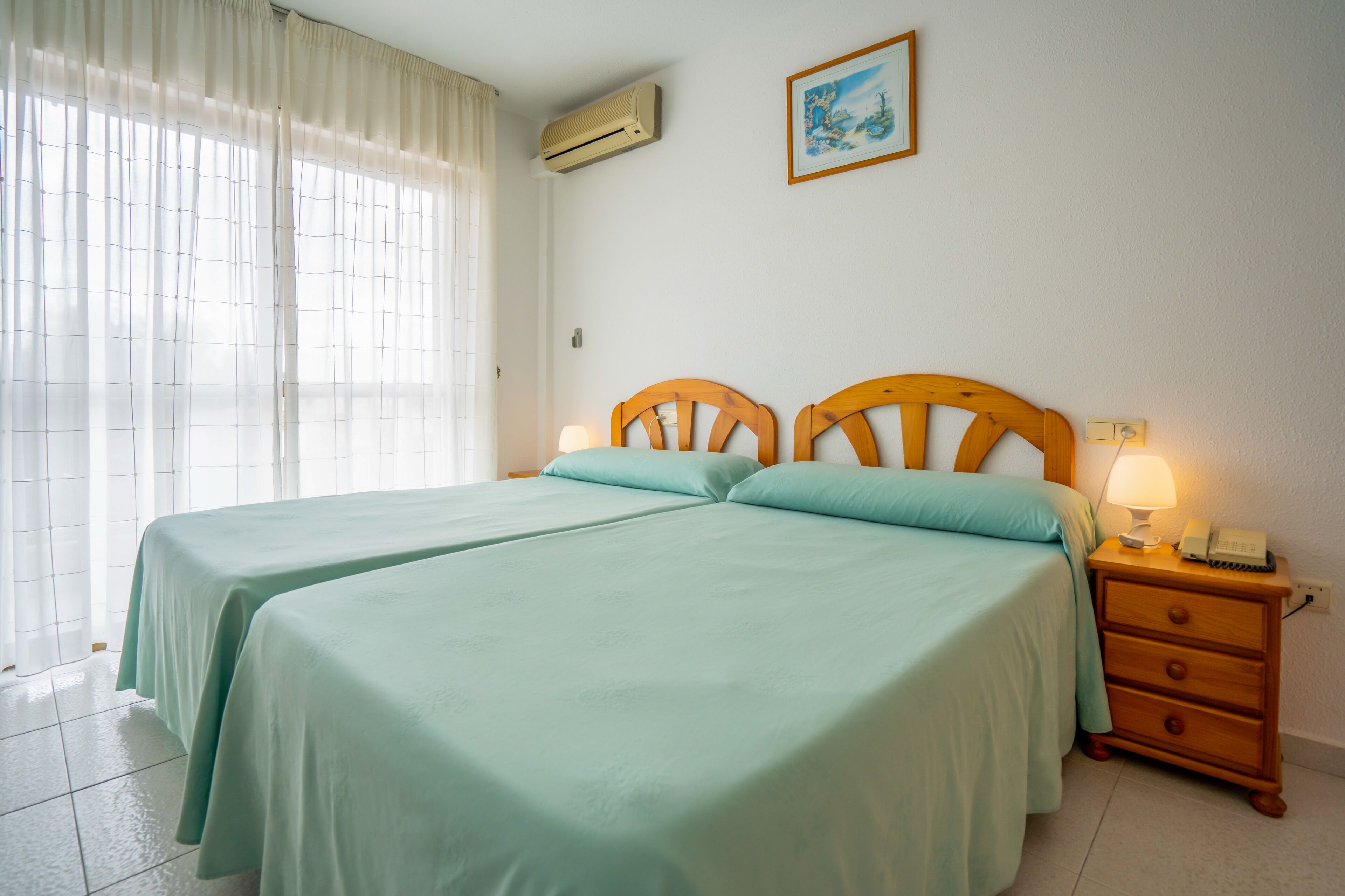 Una habitación con dos camas, una mesita de noche con lámpara y un equipo de aire acondicionado en la pared.