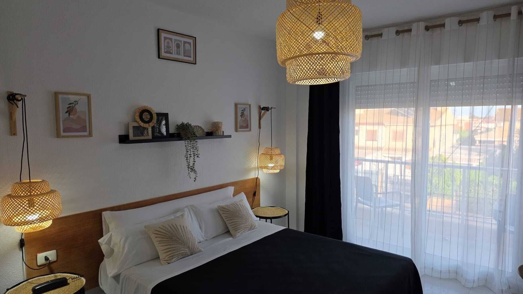 A hotel room with a bed, bedside lamps, a window with curtains, and wall decorations.
