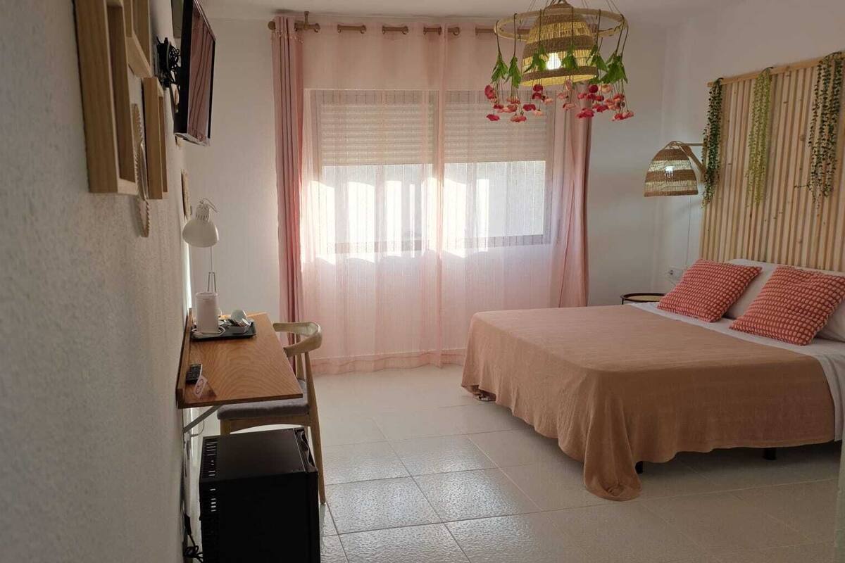 A bedroom with a bed, a desk, a chair, a lamp, and a window with curtains.