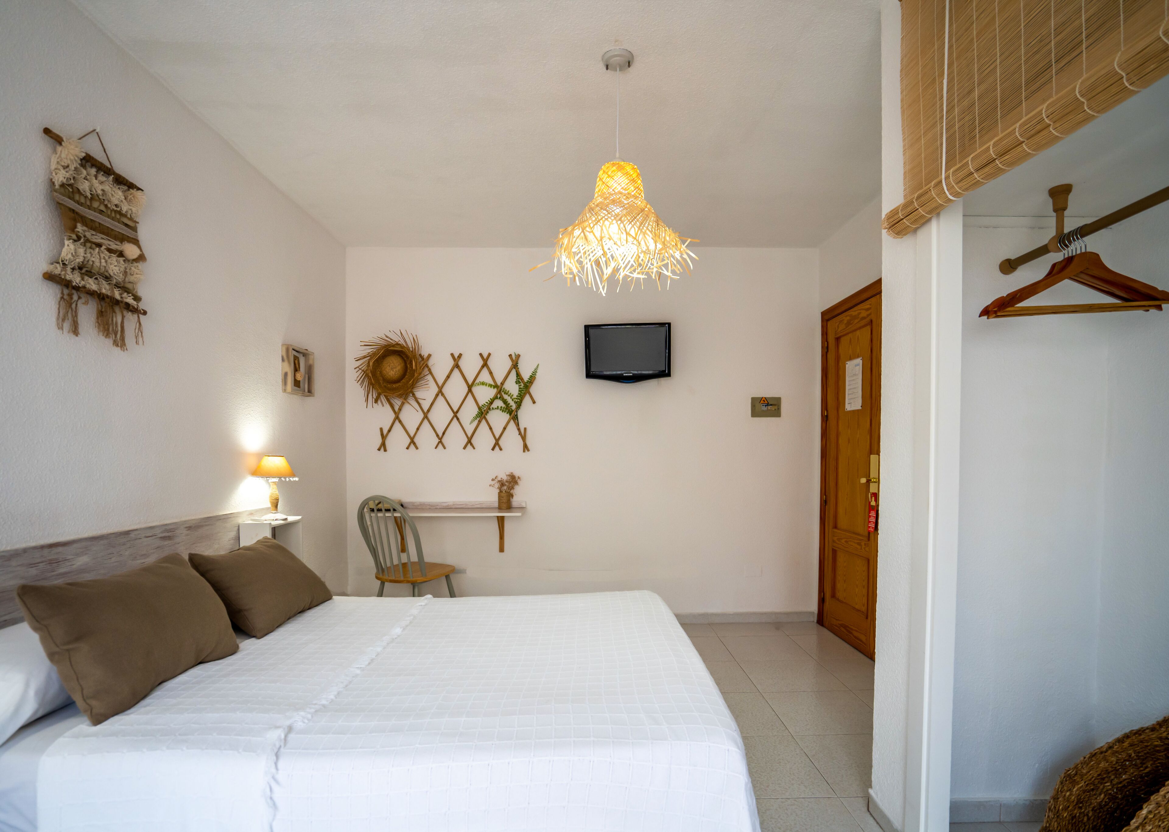 A bedroom with a bed, a chair, a TV, and a hanging light fixture.