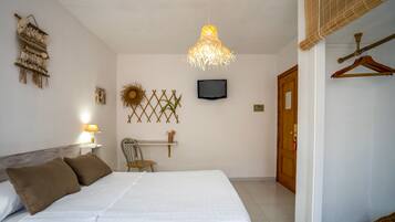 A bedroom with a bed, a chair, a TV, and a hanging light fixture.