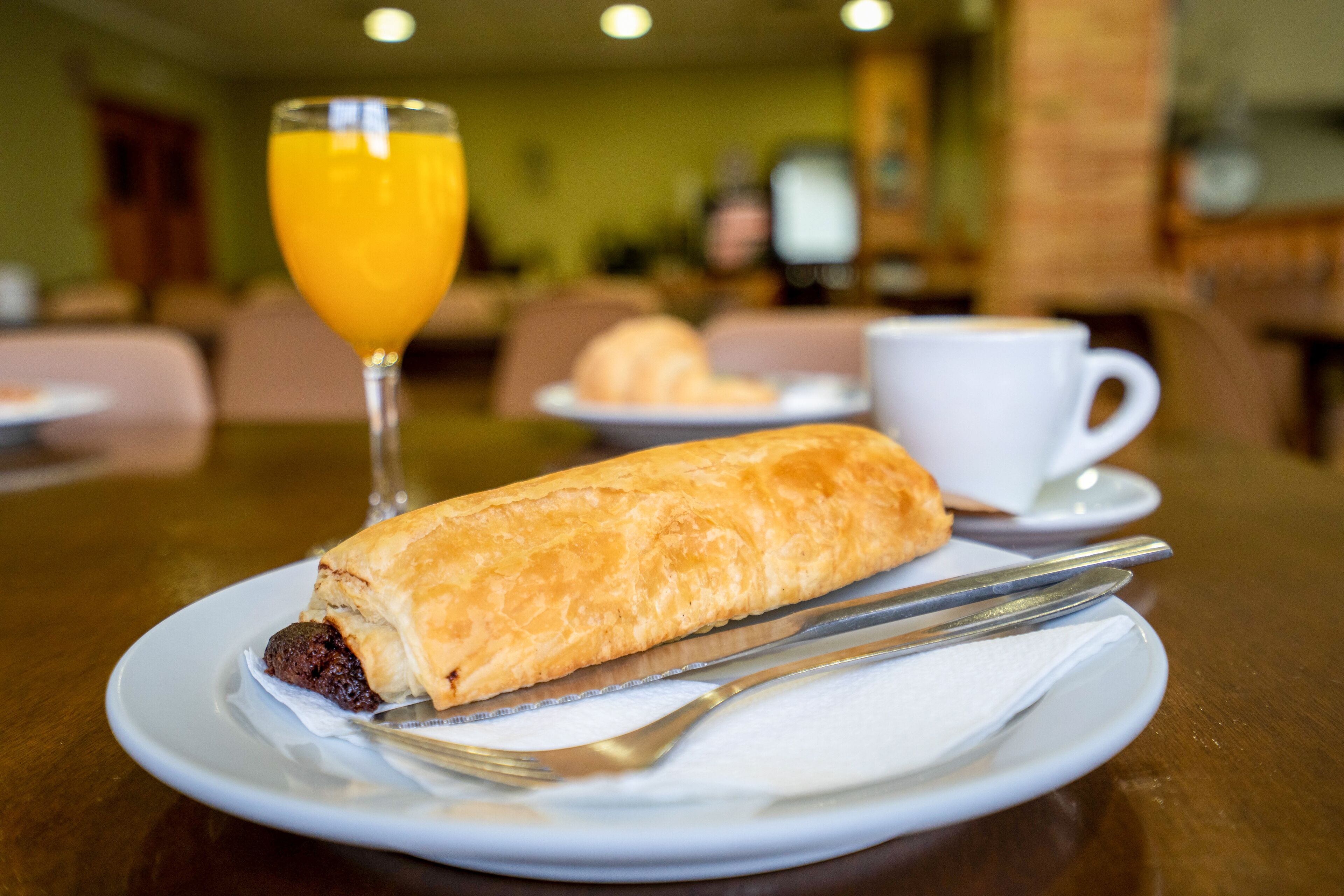 A breakfast setting with a pastry, a glass of orange juice, and a cup of coffee on a table.