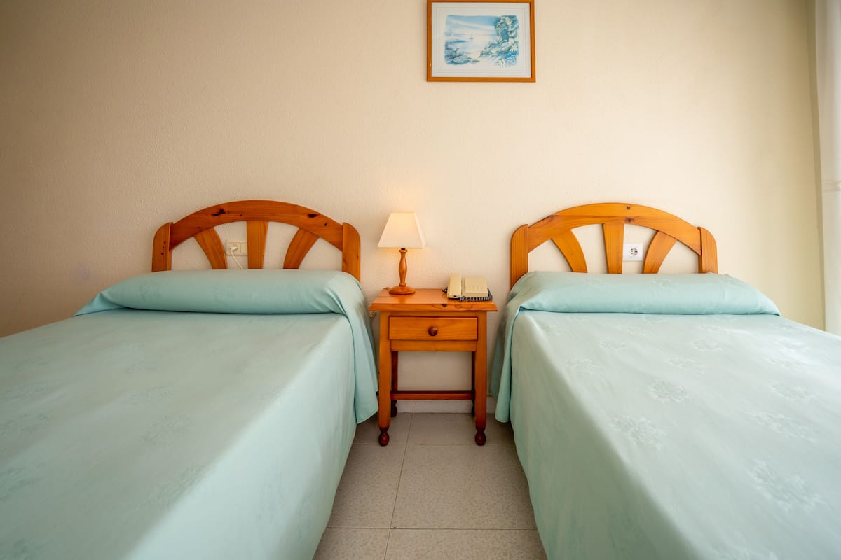 Una habitación con dos camas individuales, una mesita de noche con lámpara y un cuadro en la pared.