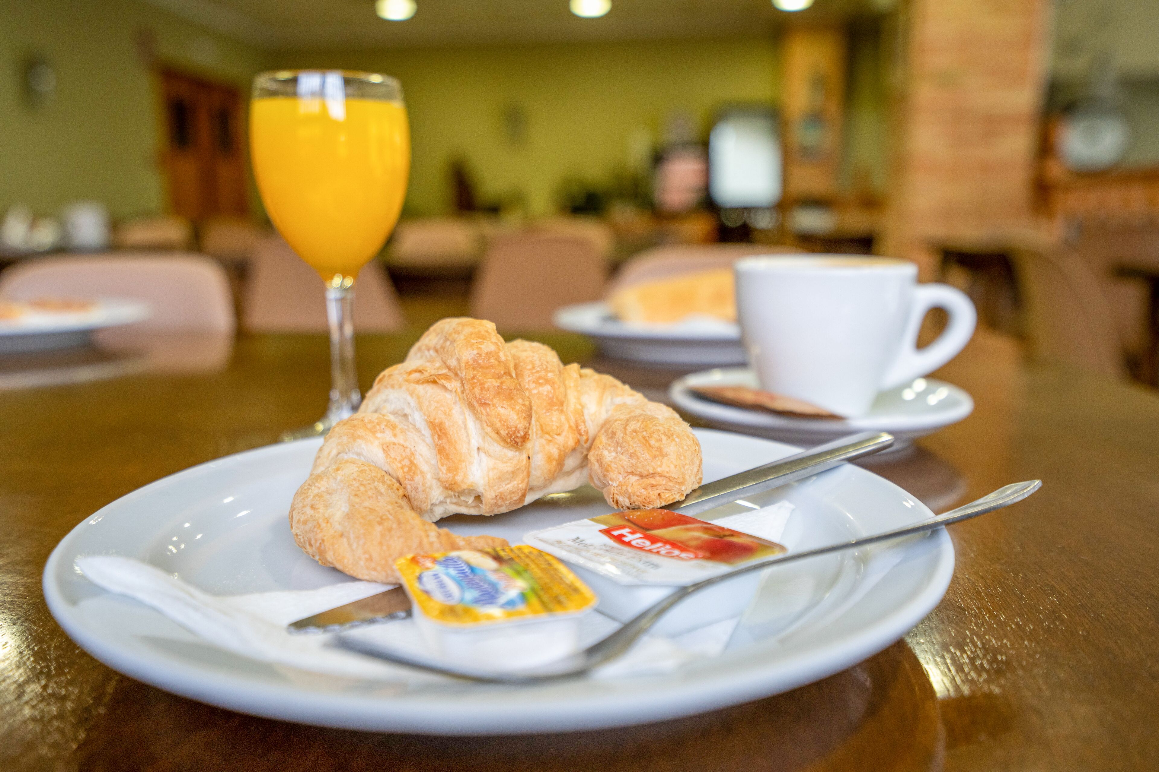 A breakfast setting with a croissant, a glass of orange juice, a cup, and a plate with a butter knife and a packet of butter.