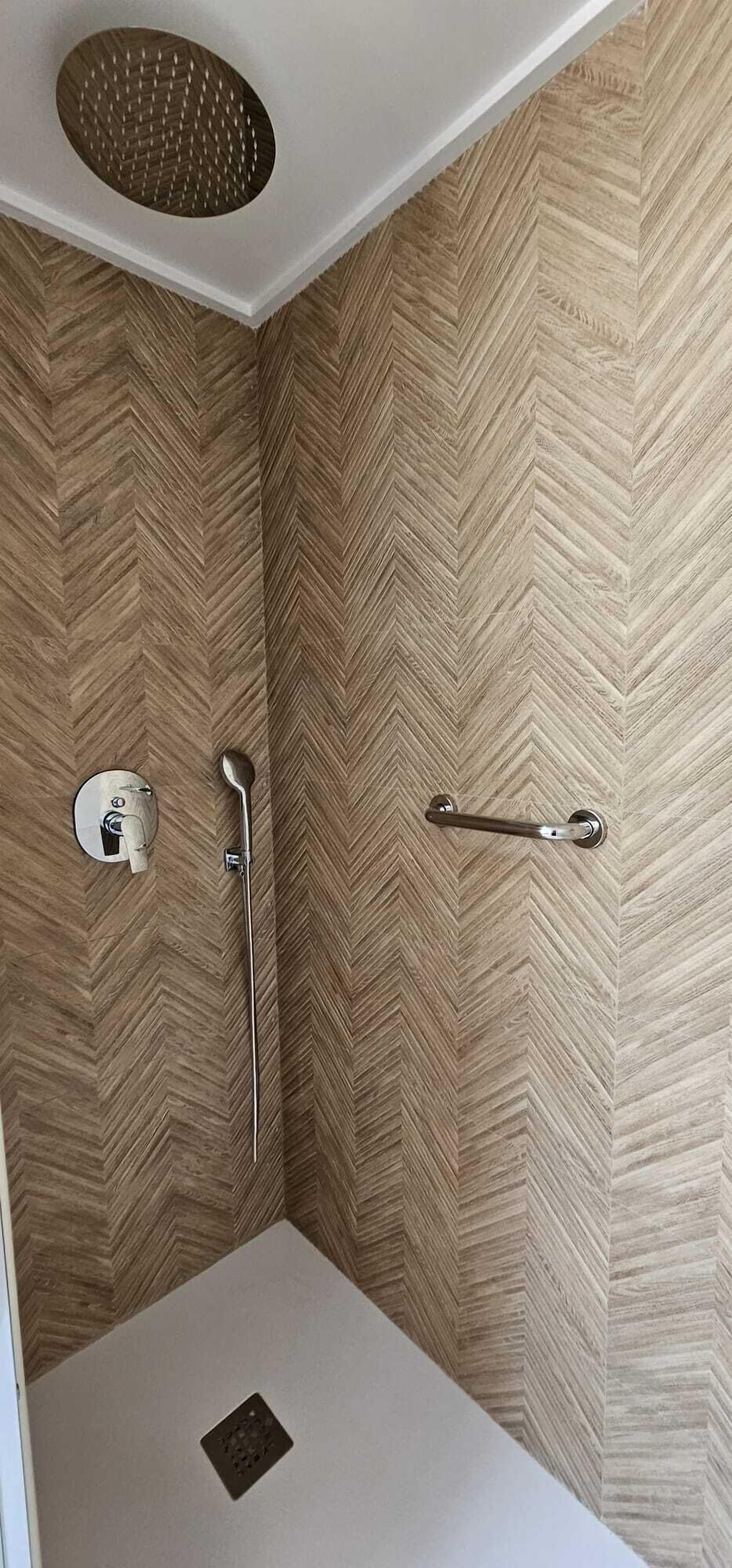 A shower with a herringbone-patterned wall, a handheld showerhead, and a handheld towel bar.