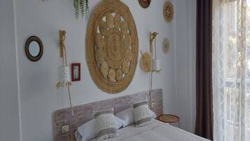 Une chambre à coucher comprenant un lit, deux tables de chevet, un téléphone fixé au mur et divers objets décoratifs, notamment des éléments de décoration murale tissés et une plante suspendue.