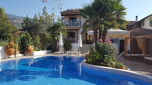 A swimming pool with a tiled edge, surrounded by potted plants and outdoor furniture. - Enalion Hotel (South Pelion)