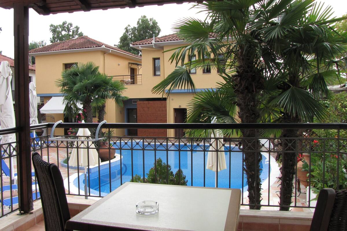 A balcony with a view of a swimming pool, a table, and chairs.