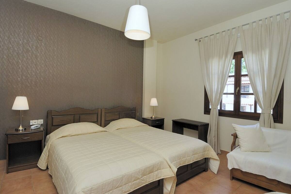 A bedroom with a large bed, two bedside tables with lamps, a window with curtains, and a wooden headboard.
