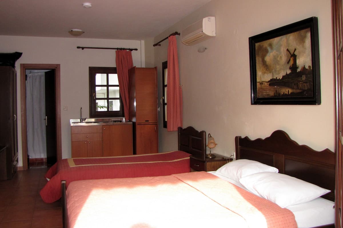 A hotel room with a bed, a desk, a chair, a wardrobe, a window with curtains, and a painting on the wall.