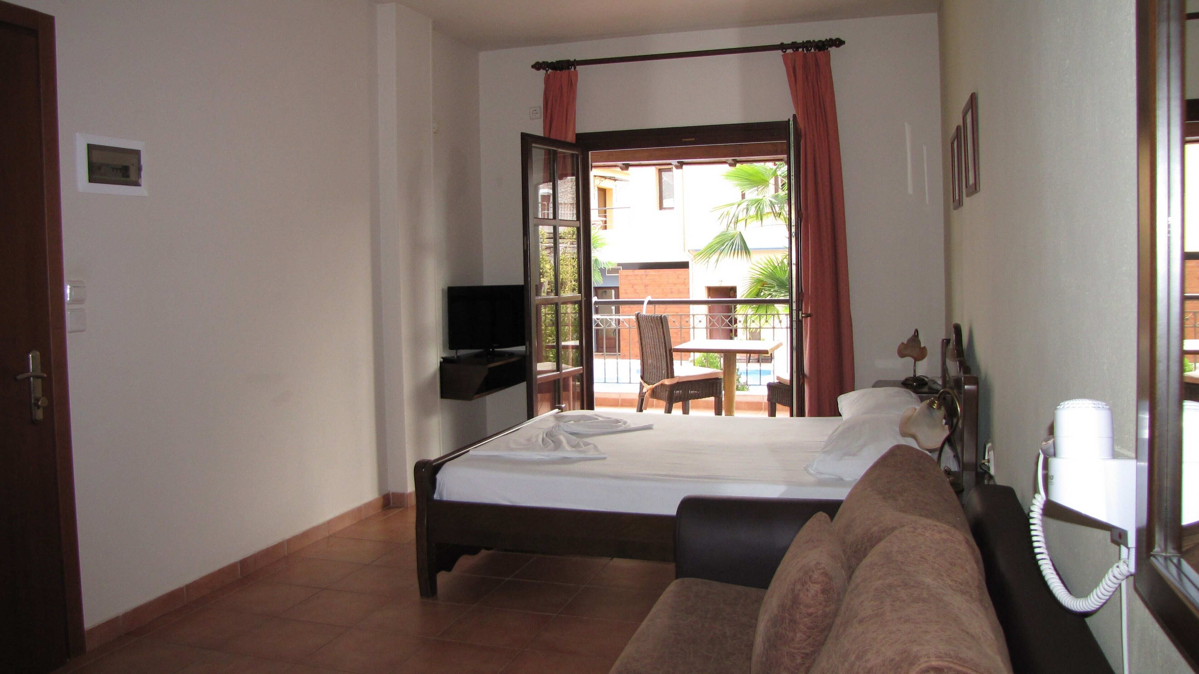 Ein Hotelzimmer mit Bett, Fernseher, Sofa, Telefon und Blick auf den Außenbalkon.