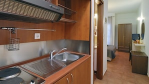 A compact kitchen with a sink, stove, and overhead ventilation. A small dining area with a table and chairs is visible in the background. - Enalion Hotel (South Pelion)