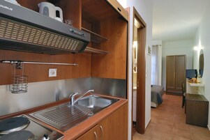 Cocina compacta con fregadero, estufa y campana extractora. En el fondo, se aprecia un pequeño comedor con mesa y sillas.