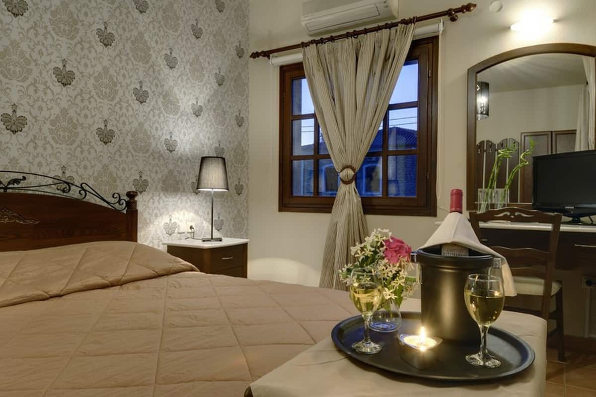 A hotel room with a bed, a bedside table with a lamp, a window with curtains, a tray with a wine glass, and a television.