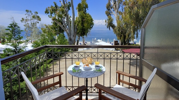 A balcony with a table set for breakfast, overlooking a beach with lounge chairs and umbrellas. - Enalion Hotel (South Pelion)