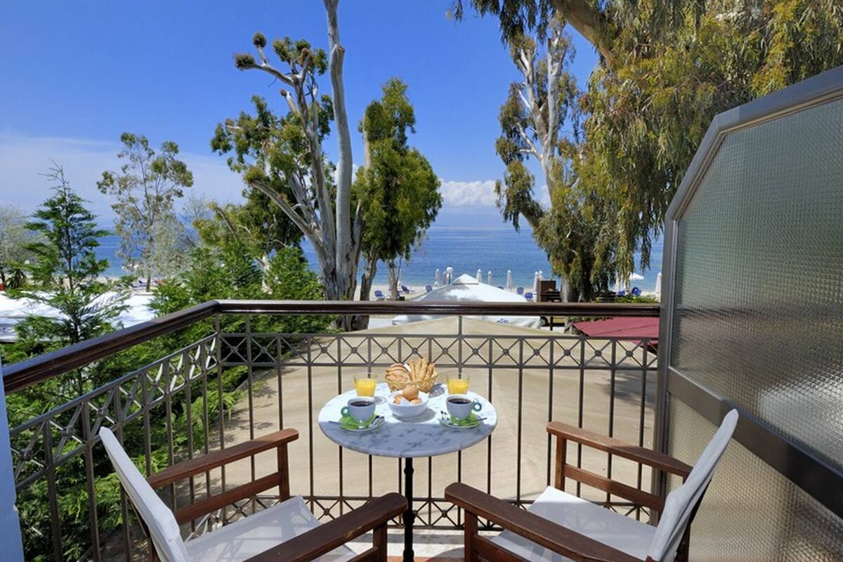A balcony with a table set for breakfast, overlooking a beach with lounge chairs and umbrellas.