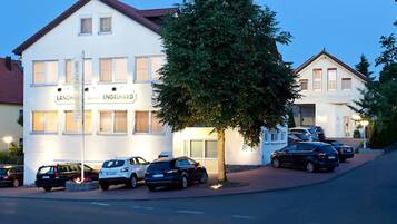 Un edificio blanco con el letrero "LANDHOF ENGELHARD", coches estacionados y un árbol en frente.