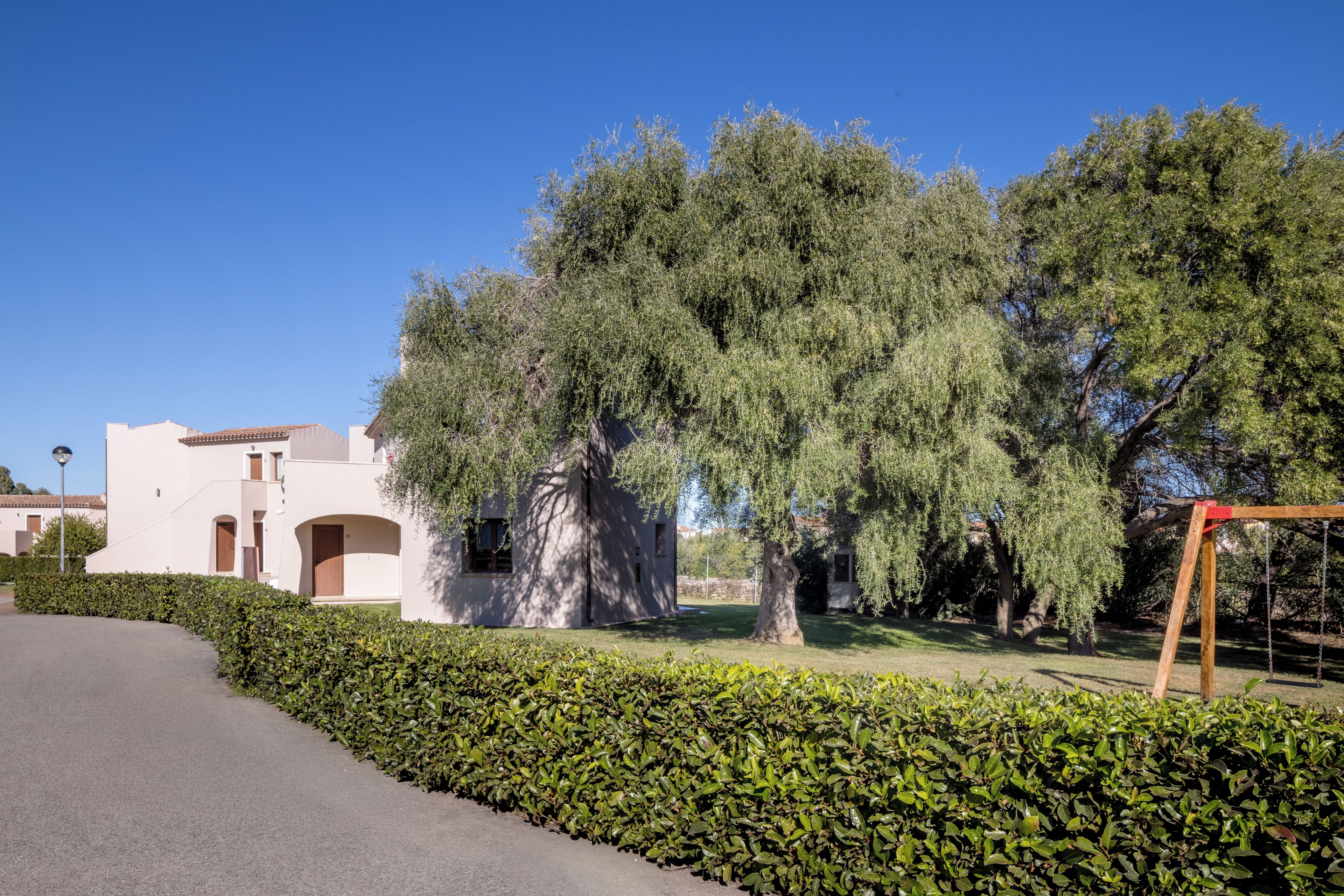 A residential area with a white building, a hedge, and trees.