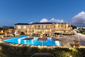 Un hotel con una piscina grande, mobiliario exterior y una fachada bien iluminada.